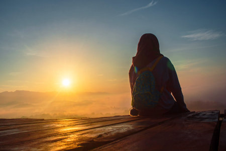 A woman in hijab Enjoying the beauty of a romantic Sunrise with golden skies and thin clouds at...