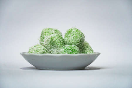Indonesian snacks made from green glutinous rice and inside there is brown sugar, small round shape with grated coconut topping, served in a small bowl on a white backgroundの写真素材