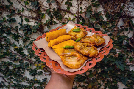 A plate of fried food in hand which is a favorite snack such as risol, spring rolls, martabak and...