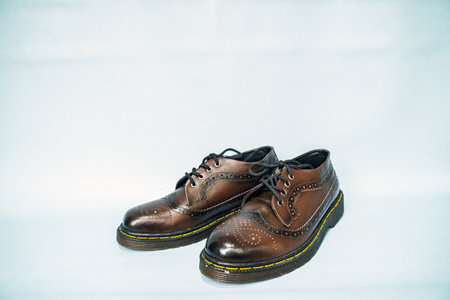 Wingtip brogue full dark brown shoe with black gradation, made of genuine cowhide with rubber sole, has detailed pattern and shiny color with white tosca backgroundの写真素材
