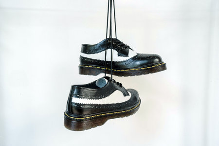 Two tone black and white wingtip brogue shoes with rubber sole hanging by laces on a white background. Nice details of premium quality handmade classic shoes made by local artisansの写真素材