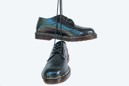 Full black wingtip brogue shoes with rubber sole hanging by laces on a white background. Nice details of premium quality handmade classic shoes made by local artisansの写真素材
