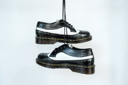 Two tone black and white wingtip brogue shoes with rubber sole hanging by laces on a white background. Nice details of premium quality handmade classic shoes made by local artisansの写真素材