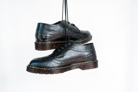 Full black wingtip brogue shoes with rubber sole hanging by laces on a white background. Nice details of premium quality handmade classic shoes made by local artisansの写真素材