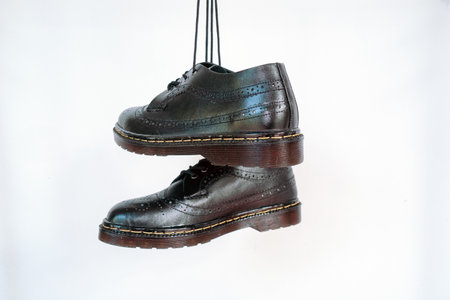 Full black wingtip brogue shoes with rubber sole hanging by laces on a white background. Nice details of premium quality handmade classic shoes made by local artisansの写真素材