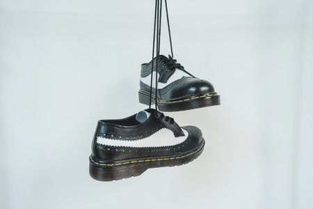 Two tone black and white wingtip brogue shoes with rubber sole hanging by laces on a white background. Nice details of premium quality handmade classic shoes made by local artisansの写真素材