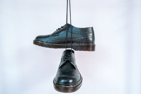 Full black wingtip brogue shoes with rubber sole hanging by laces on a white background. Nice details of premium quality handmade classic shoes made by local artisansの写真素材