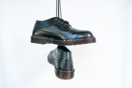 Full black wingtip brogue shoes with rubber sole hanging by laces on a white background. Nice details of premium quality handmade classic shoes made by local artisansの写真素材