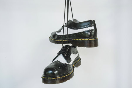 Two tone black and white wingtip brogue shoes with rubber sole hanging by laces on a white background. Nice details of premium quality handmade classic shoes made by local artisansの写真素材