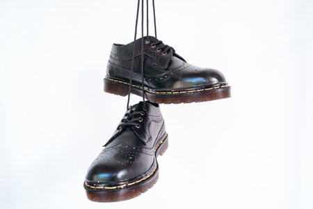 Full black wingtip brogue shoes with rubber sole hanging by laces on a white background. Nice details of premium quality handmade classic shoes made by local artisansの写真素材