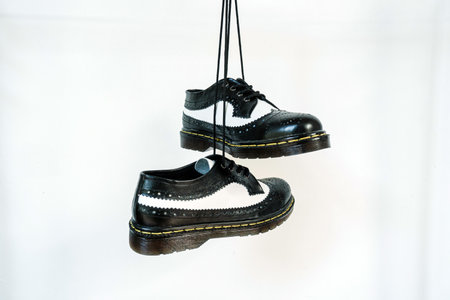 Two tone black and white wingtip brogue shoes with rubber sole hanging by laces on a white background. Nice details of premium quality handmade classic shoes made by local artisansの写真素材