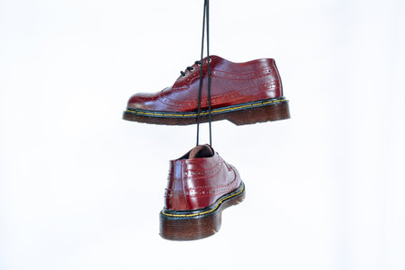 Full maroon wingtip brogue shoes with rubber sole hanging by laces on a white background. Nice details of premium quality handmade classic shoes made by local artisansの写真素材