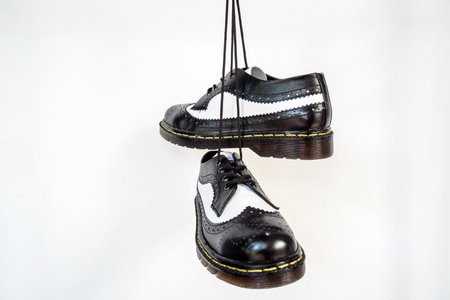 Two tone black and white wingtip brogue shoes with rubber sole hanging by laces on a white background. Nice details of premium quality handmade classic shoes made by local artisansの写真素材