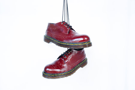 Full maroon wingtip brogue shoes with rubber sole hanging by laces on a white background. Nice details of premium quality handmade classic shoes made by local artisansの写真素材