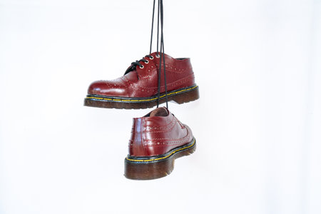 Full maroon wingtip brogue shoes with rubber sole hanging by laces on a white background. Nice details of premium quality handmade classic shoes made by local artisansの写真素材