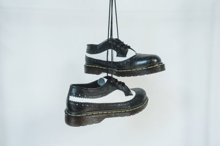 Two tone black and white wingtip brogue shoes with rubber sole hanging by laces on a white background. Nice details of premium quality handmade classic shoes made by local artisansの写真素材