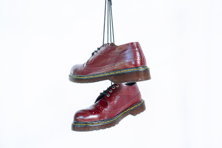 Full maroon wingtip brogue shoes with rubber sole hanging by laces on a white background. Nice details of premium quality handmade classic shoes made by local artisansの写真素材