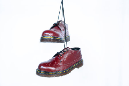 Full maroon wingtip brogue shoes with rubber sole hanging by laces on a white background. Nice details of premium quality handmade classic shoes made by local artisansの写真素材