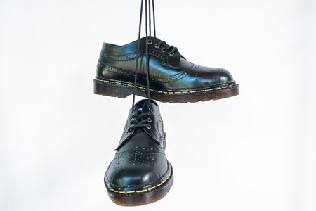 Full black wingtip brogue shoes with rubber sole hanging by laces on a white background. Nice details of premium quality handmade classic shoes made by local artisansの写真素材