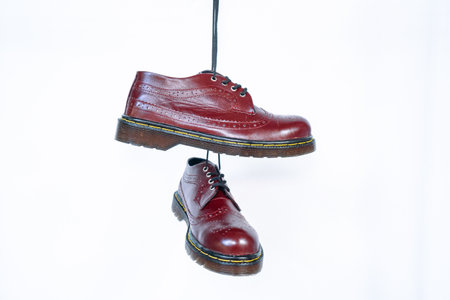Full maroon wingtip brogue shoes with rubber sole hanging by laces on a white background. Nice details of premium quality handmade classic shoes made by local artisansの写真素材