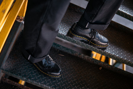 Close-up view of concept photo of full black wingtip brogue shoes made of genuine leather worn by male model in scrap metal warehouseの写真素材