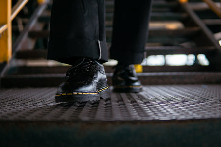 Close-up view of concept photo of full black wingtip brogue shoes made of genuine leather worn by male model in scrap metal warehouseの写真素材