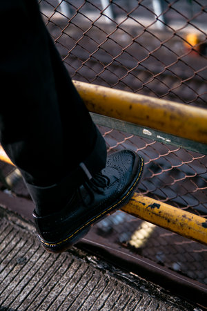 Close-up view of concept photo of full black wingtip brogue shoes made of genuine leather worn by male model in scrap metal warehouseの写真素材