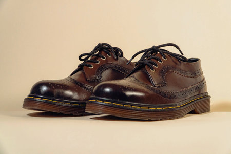 Close up of dark brown brogue wingtip shoes with rubber outsole made from genuine cow leather. Studio shot of an elegant and shiny vintage shoe product on a beige backgroundの写真素材