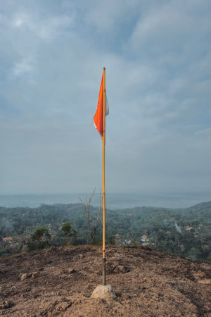 The peak of the ancient volcano Nglanggeran is dominated by rocks & contains the red and white Indonesian flag. Photo of rocky mountain peak with waving flag on a tropical morningの写真素材