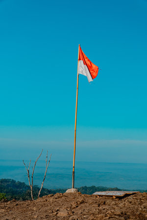 The peak of the ancient volcano Nglanggeran is dominated by rocks & contains the red and white Indonesian flag. Photo of rocky mountain peak with waving flag on a tropical morningの写真素材