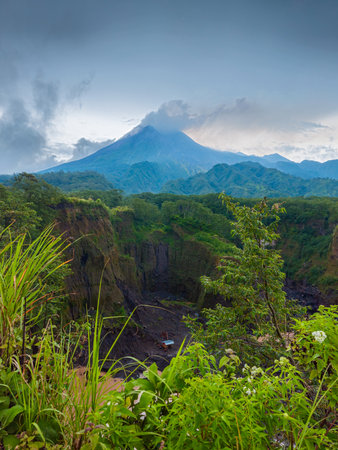 Panorama of Mount Merapi from a close distance with rows of clouds around it in the afternoon. Landscape of active volcano in detail from south side with rocks and ravine in frontの写真素材
