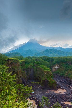 Panorama of Mount Merapi from a close distance with rows of clouds around it in the afternoon. Landscape of active volcano in detail from south side with rocks and ravine in frontの写真素材