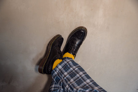 Close-up of the legs of a man wearing blue tartan trousers combined with jet black genuine leather...