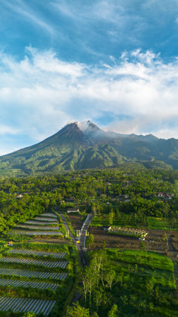 Aerial view of a volcano in the morning with a view of the forest and a branching road in front. Drone footage shows the beauty of Mount Merapi in Yogyakarta, Indonesia at sunriseの写真素材