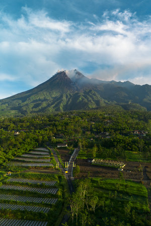 Aerial view of a volcano in the morning with a view of the forest and a branching road in front. Drone footage shows the beauty of Mount Merapi in Yogyakarta, Indonesia at sunriseの写真素材