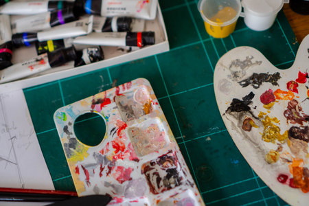 A paint palette that is used too often causes the paint to dry out and build up. Close-up of a paint palette and other painting supplies scattered on the tableの写真素材
