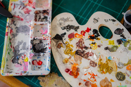 A paint palette that is used too often causes the paint to dry out and build up. Close-up of a paint palette and other painting supplies scattered on the tableの写真素材