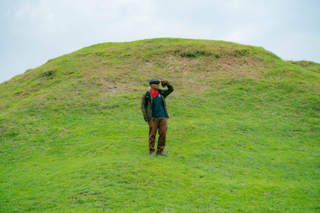A male adventurer is enjoying the beauty of the expanse of green grass. The Asian male traveler relaxes and is amazed by the natural charm of the clean and beautiful green hills.の写真素材