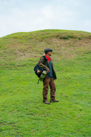 A male adventurer is enjoying the beauty of the expanse of green grass. The Asian male traveler relaxes and is amazed by the natural charm of the clean and beautiful green hills.の写真素材