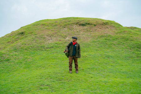 A male adventurer is enjoying the beauty of the expanse of green grass. The Asian male traveler relaxes and is amazed by the natural charm of the clean and beautiful green hills.の写真素材