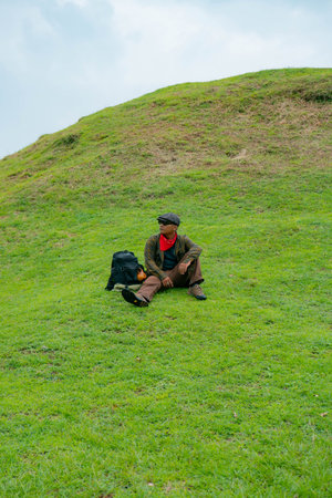 An adventurer is resting by sitting on a stretch of green grass hill. Asian male travelers enjoy the...