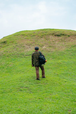 A male adventurer is enjoying the beauty of the expanse of green grass. The Asian male traveler relaxes and is amazed by the natural charm of the clean and beautiful green hills.の写真素材