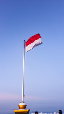 The Indonesian national flag on a mountaintop against a clear blue sky in the morning. Close-up of...