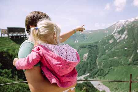 Young father carrying his little daughter and showing her the beauty of the Georgian mountainsの写真素材