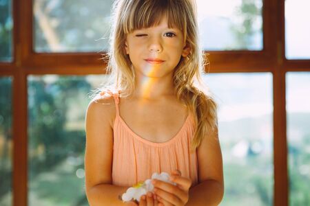 Little girl holding a flower in her hands. A rainbow on her faceの写真素材