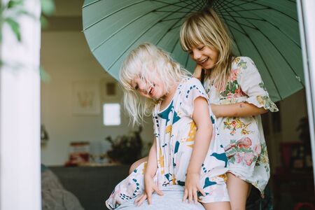 Two little girl having fun at home with a big umbrella above themの写真素材