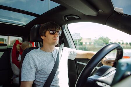 Father driving a car with his little daughter at the back seat in a child sitの写真素材