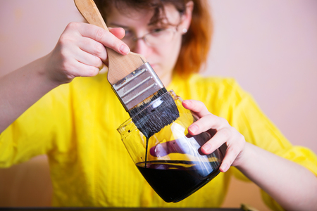 A woman dabs a paintbrush in the dark paint in the jar. Creation. Craft and artの写真素材