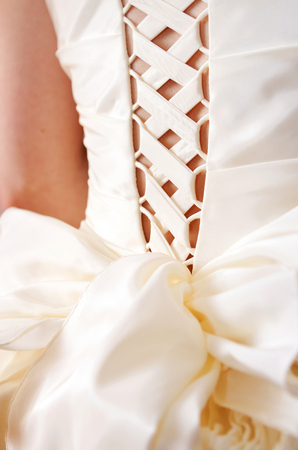 Wide satin lacing on the wedding dress of the bride. The ribbon is tied in a lush bow. View from the back.の写真素材