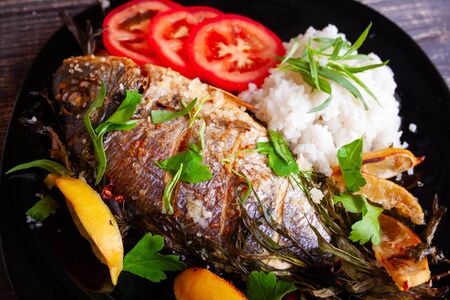Baked dorada fish with lemon, parsley, rosemary and tomatoes with a side dish of boiled riceの写真素材